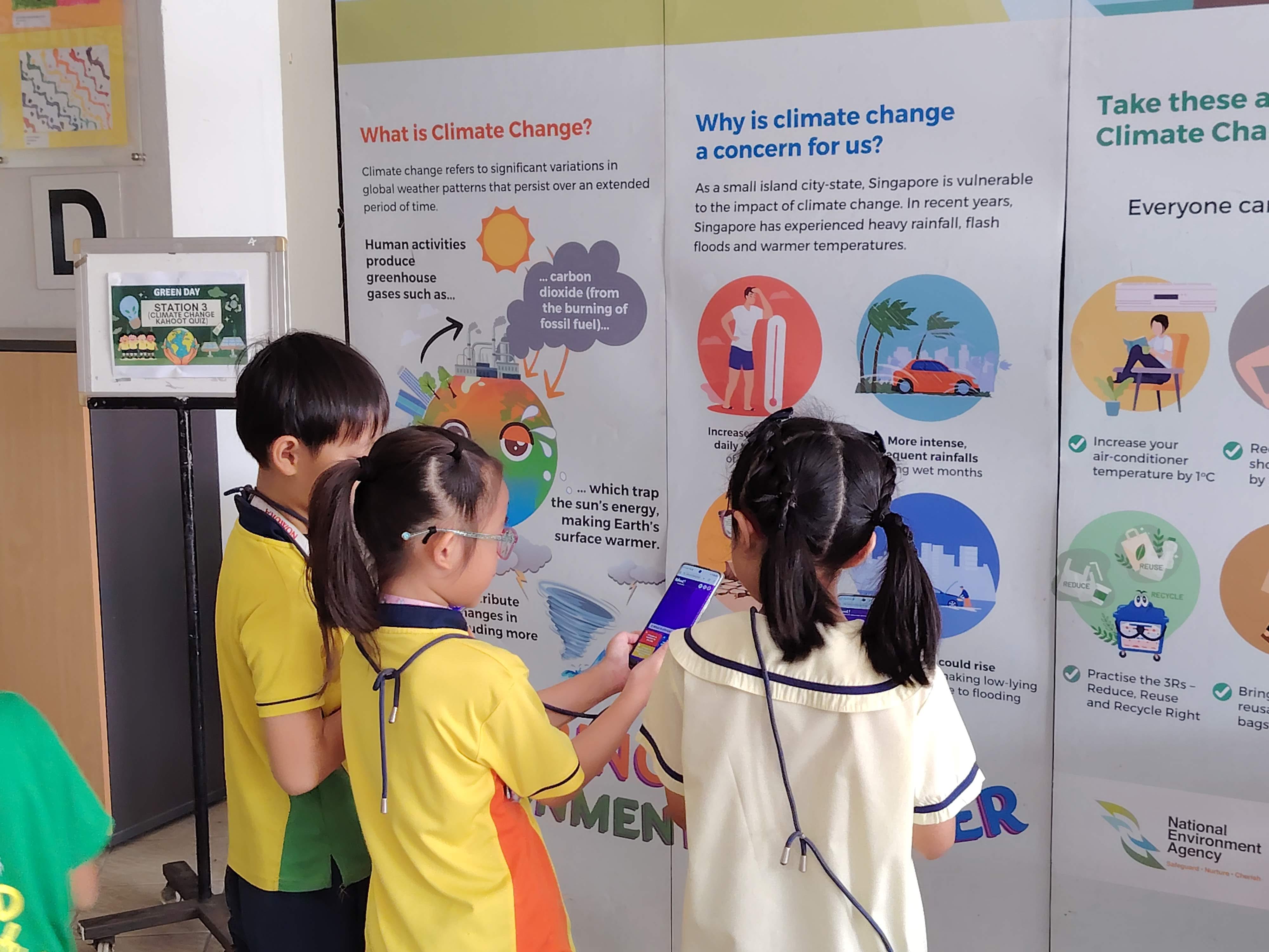 Three students standing in front of a colorful climate change educational display as they attempt to complete a quiz